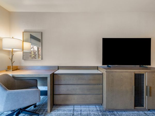 A modern office setup with a desk, chair, lamp, TV, and cabinets, featuring a neutral color scheme and a simple, contemporary design.