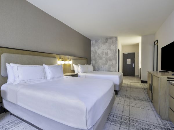 A hotel room with two neatly made double beds, a flat-screen TV, and modern decor including a patterned carpet and wall art.