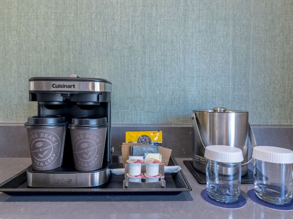 A coffee maker with cups, creamers, a tea bag, ice bucket, and glasses on a counter.