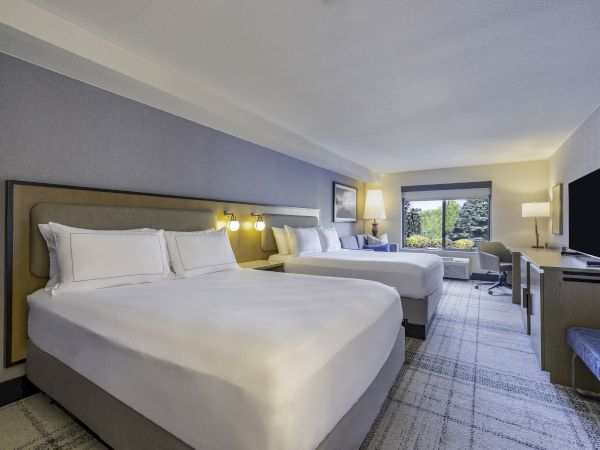 A modern hotel room with two large beds, a TV, desk, lamps, and a window showcasing greenery, creating a cozy and inviting atmosphere.