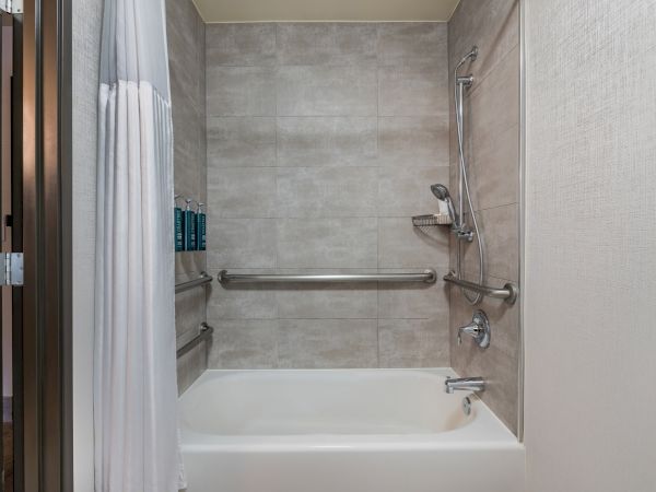 A bathroom with a bathtub, showerhead, shower curtain, and wall-mounted shampoo dispensers, featuring handrails for accessibility.